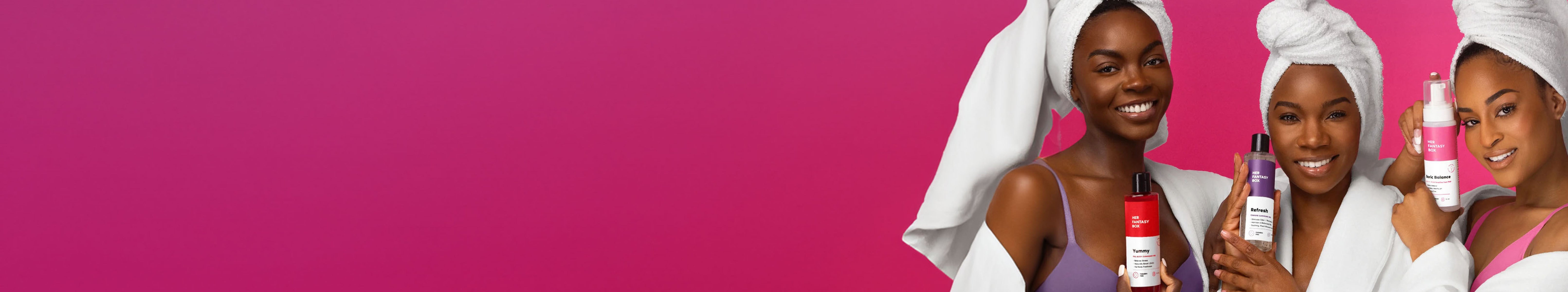 Three women with towels on their heads smiling and holding Her Fantasy Box products against a pink background.